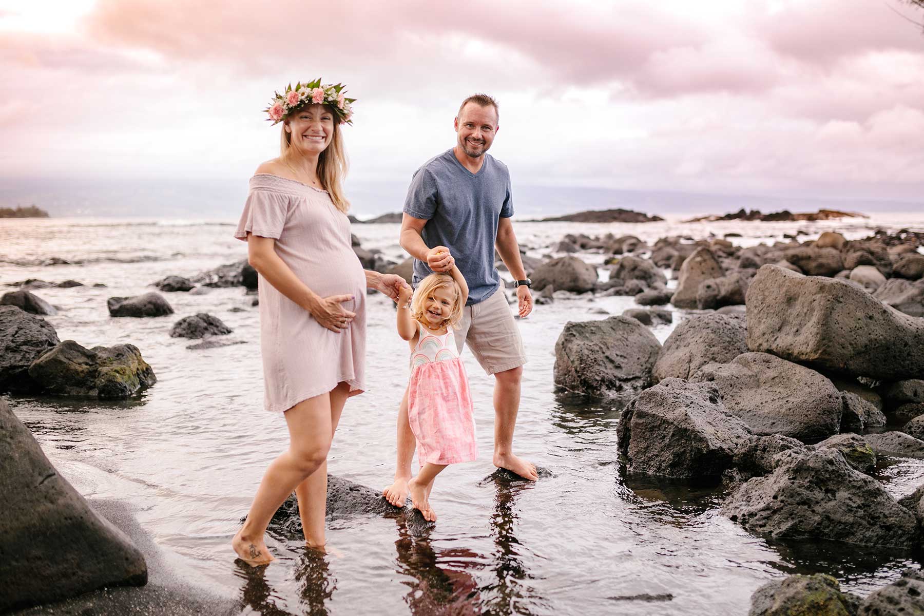 image of husband and pregnant wife walking on the beach with their daughter